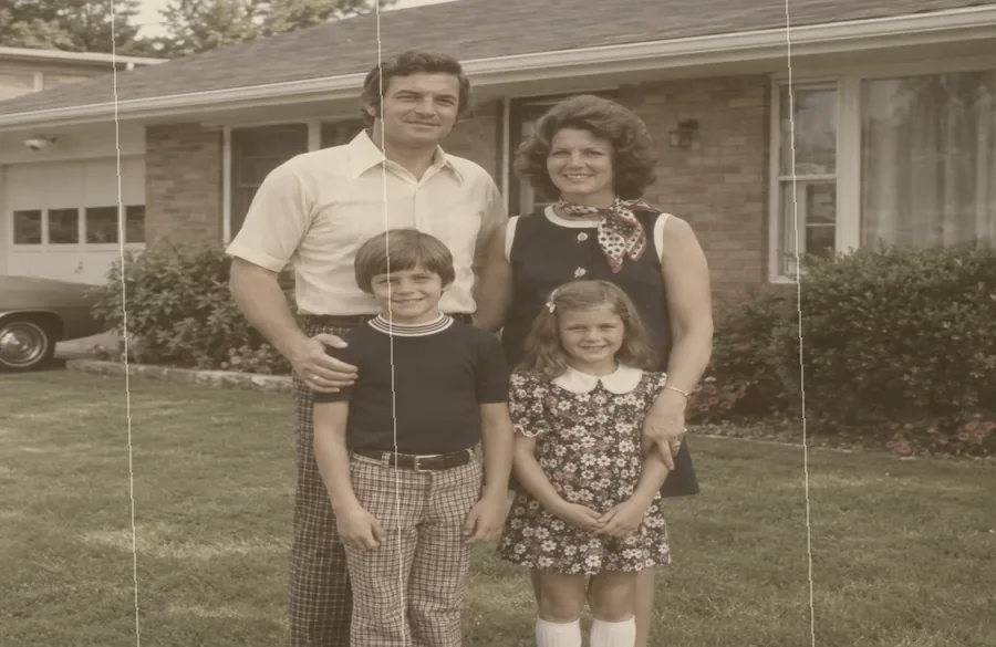 Old scanned photo of a family in front of a house, faded and scratched