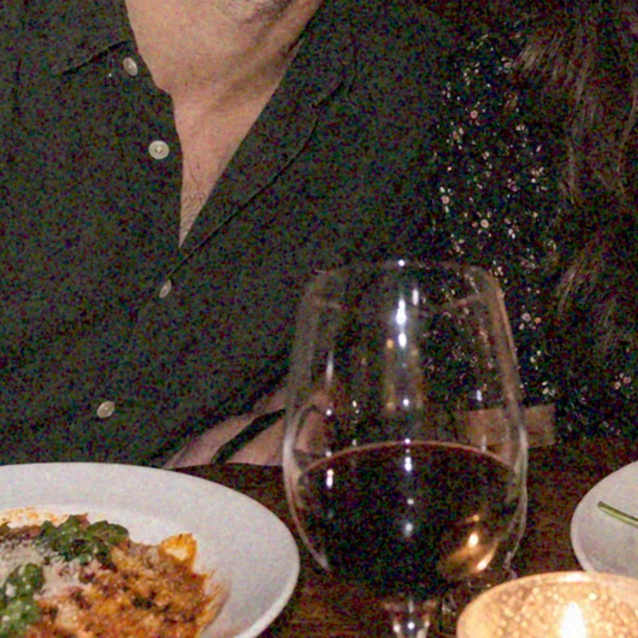 Grainy photo of a candlelit dinner table with pasta and red wine, speckled noise across the dark shirt and table