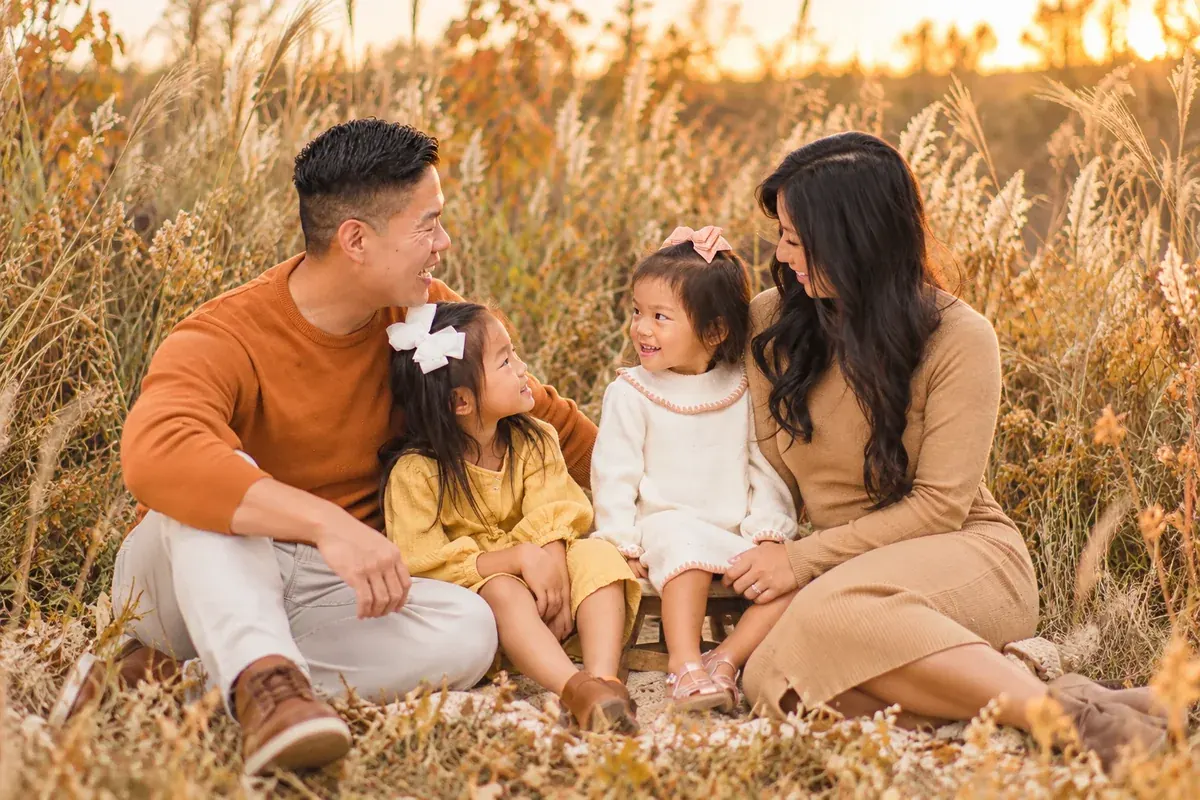 Thanksgiving family photo of parents and two daughters in coordinated rust, cream, camel and soft yellow outfits