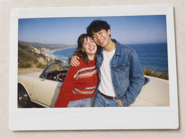 Polaroid-style AI couple photo of a young couple by the sea with a vintage car