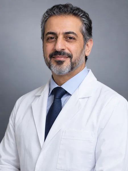 Doctor headshot of a smiling man in a white coat and tie in a bright clinic