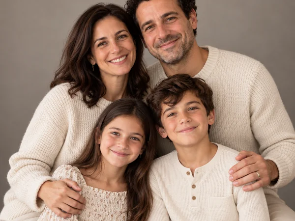 AI family portrait of parents and two children in cream outfits in a warm studio