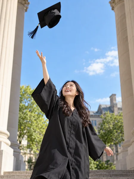 Graduate tossing her cap in the air in front of a columned university building