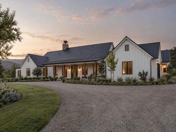 White farmhouse ranch with a dark metal roof and a gravel drive
