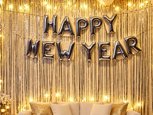 Happy New Year letter balloons over a gold tinsel curtain with cushions and lights