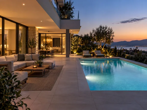 Modern villa patio beside a lit swimming pool at dusk