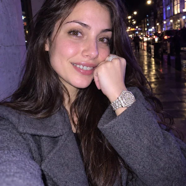 Woman with curly hair laughing with diamond grillz, an iced ring, and an iced-out watch in a night flash photo