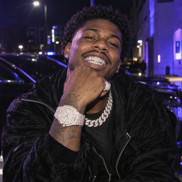 Young man grinning with diamond grillz and his fist raised to show a bust down watch