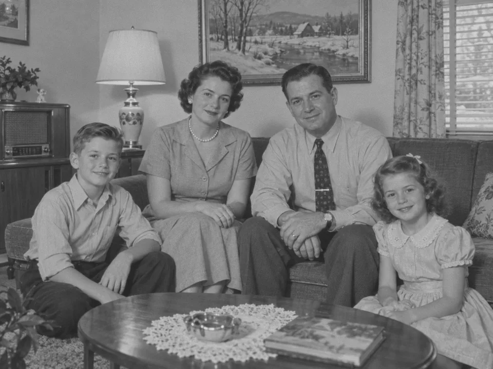 Drag to compare the black and white 1950s family photo in a living room and the colorized photo (before)
