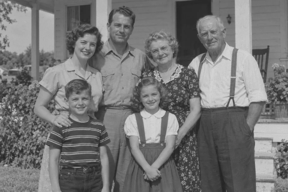 Drag to compare the black and white family photo on a porch and the colorized version with a light blue blouse and green dress (before)