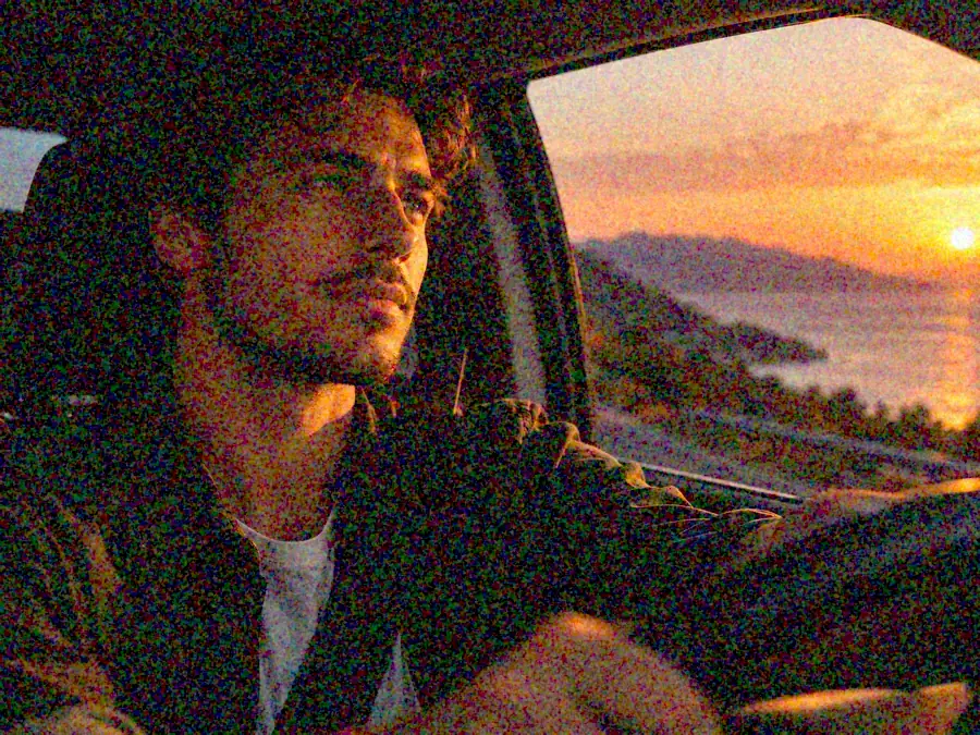 Drag to compare the grainy photo of a man driving at dusk and the denoised photo with the same face (before)