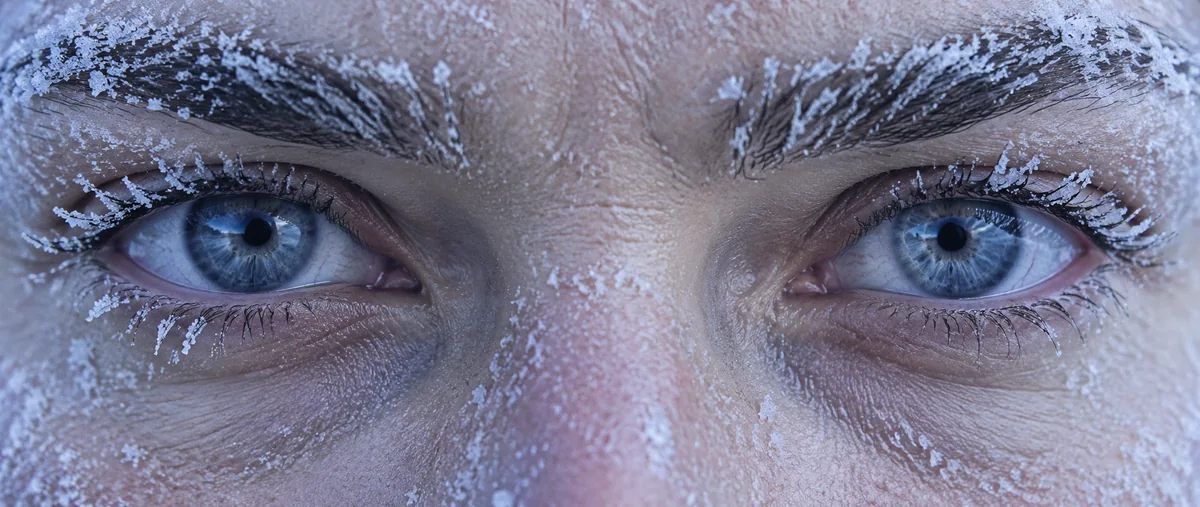 Extreme close-up of frost on eyebrows and lashes around blue eyes