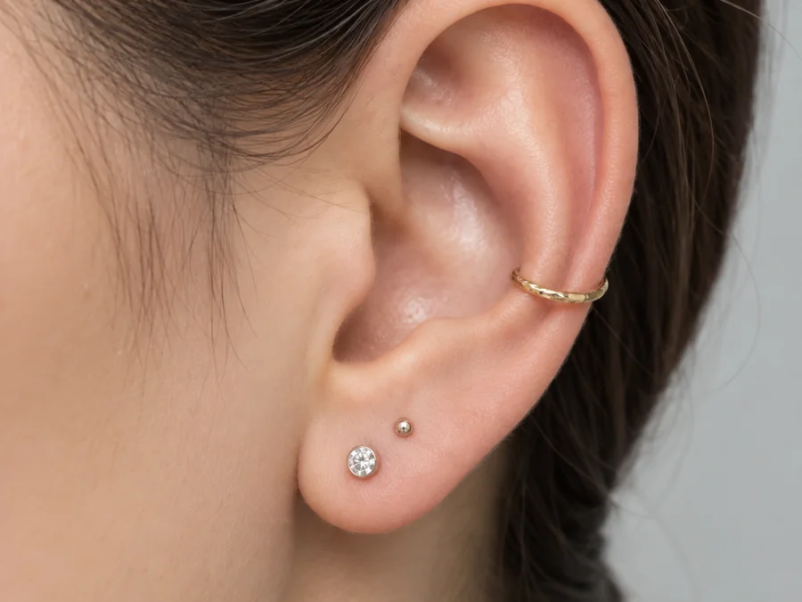 Ear with a curated stack of lobe studs, a tragus stud, and a helix hoop, with numbered placements