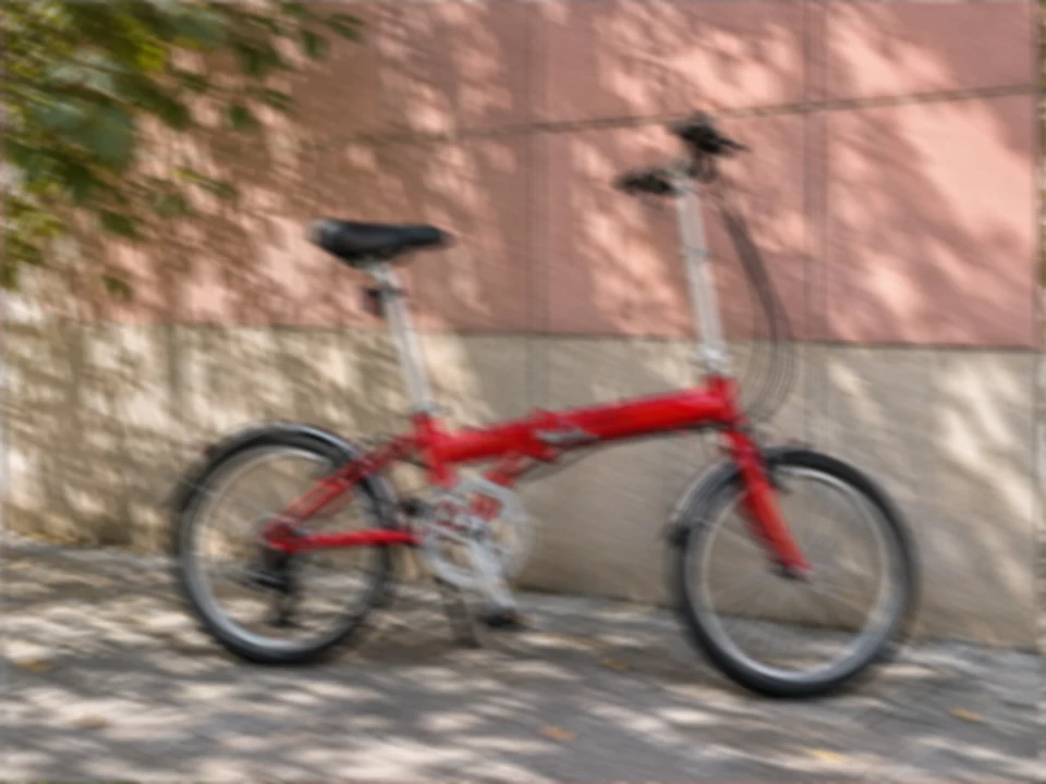 Drag to compare the shaky photo of a red folding bike and the unblurred version (before)