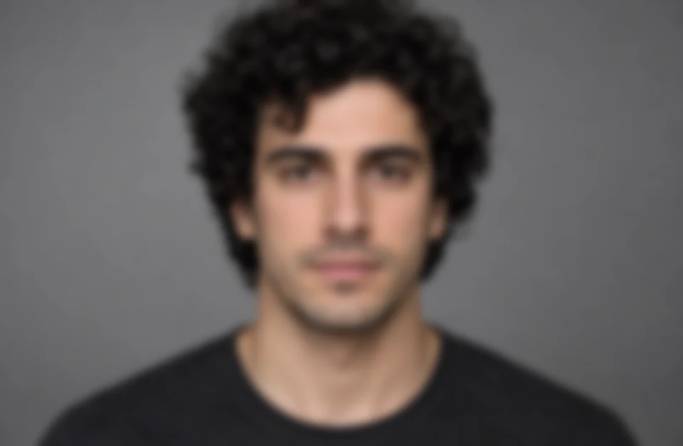 Drag to compare the out of focus face of a curly-haired man and the unblurred portrait (before)